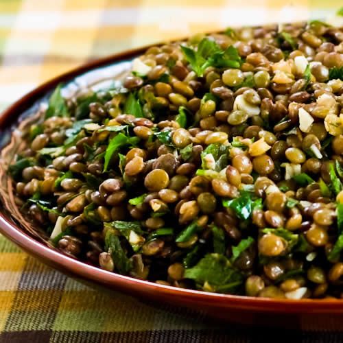 a bowl filled with lentils and greens on top of a checkered table cloth