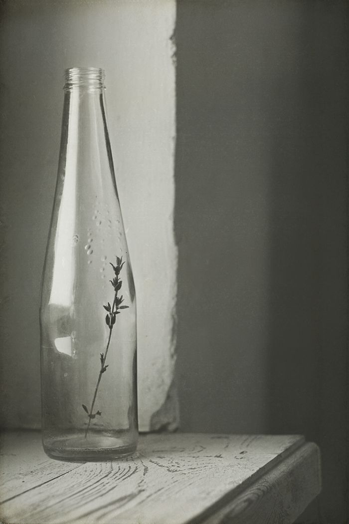 a glass bottle sitting on top of a wooden table next to a window sill