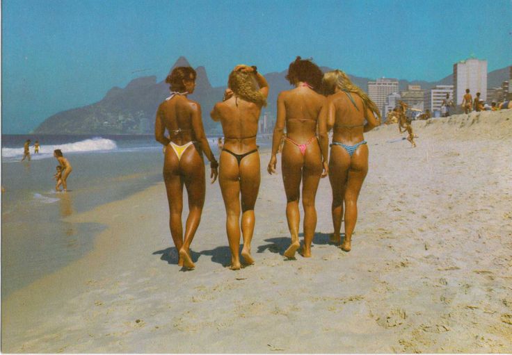 three women in bikinis walking on the beach with their backs turned to the camera