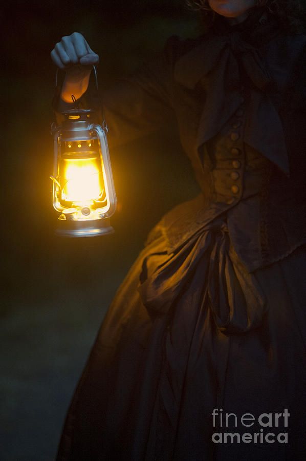 a woman in a black dress holding a lantern with yellow light on her hand and looking at the camera