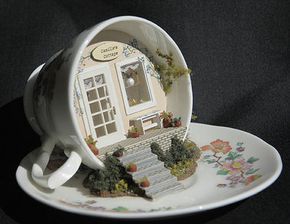 a coffee cup with a miniature house in it on top of a white saucer