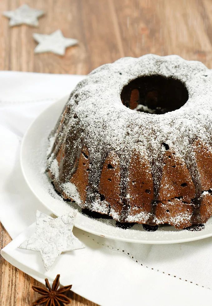 a bundt cake with powdered sugar on top sits on a white plate next to star decorations