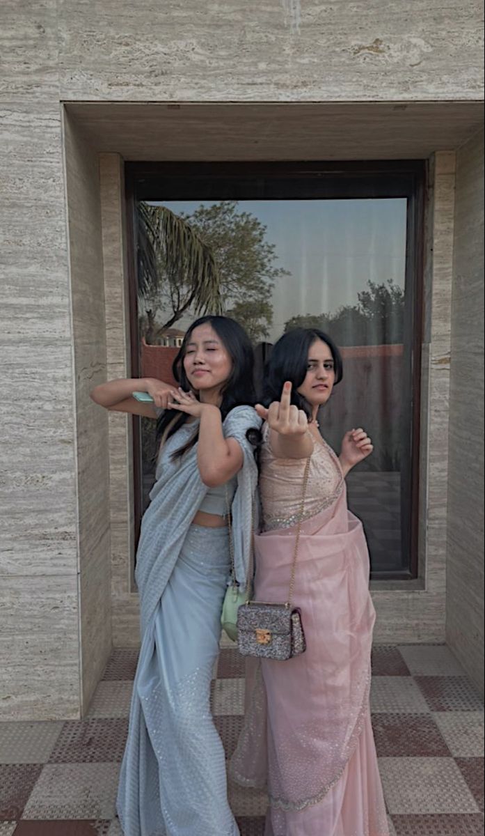 two women standing next to each other in front of a door giving the peace sign