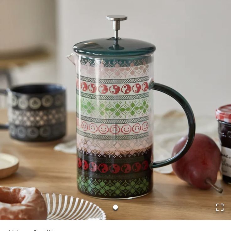 a coffee pot sitting on top of a wooden table next to donuts and apples