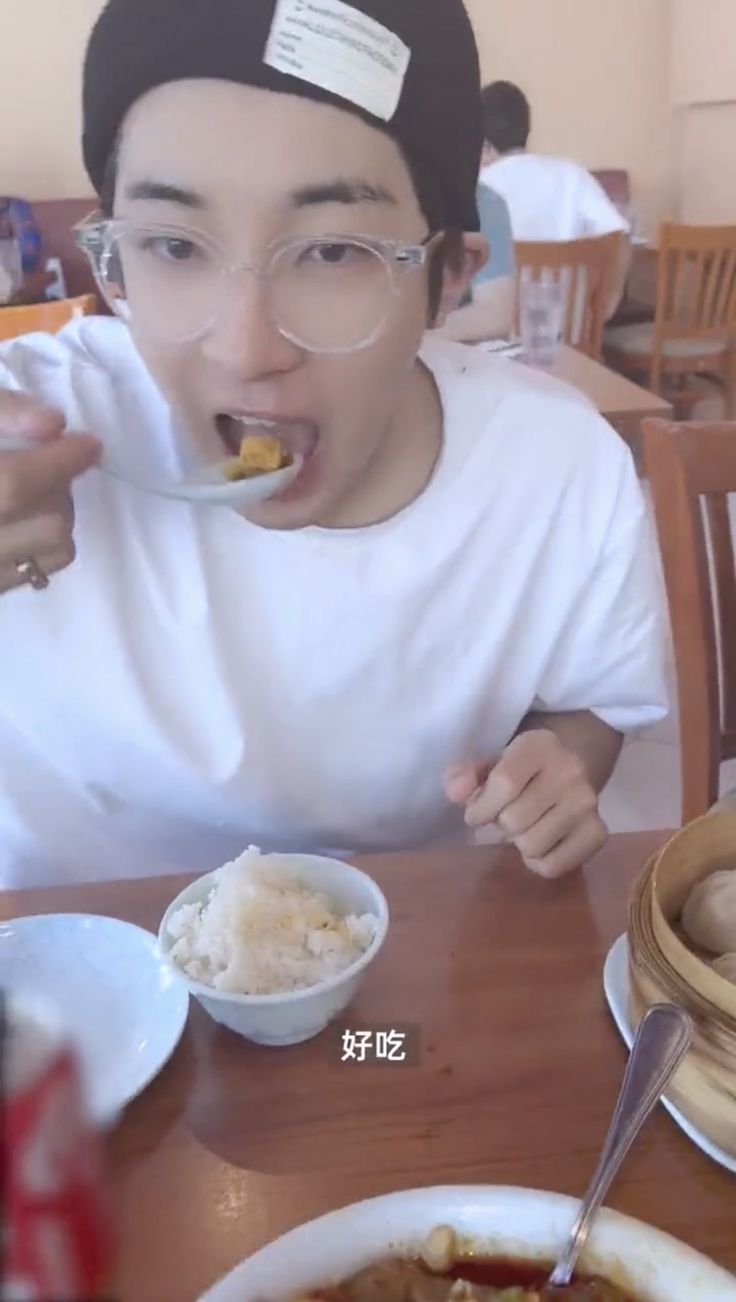 a person sitting at a table with some food in front of him and holding a spoon to their mouth