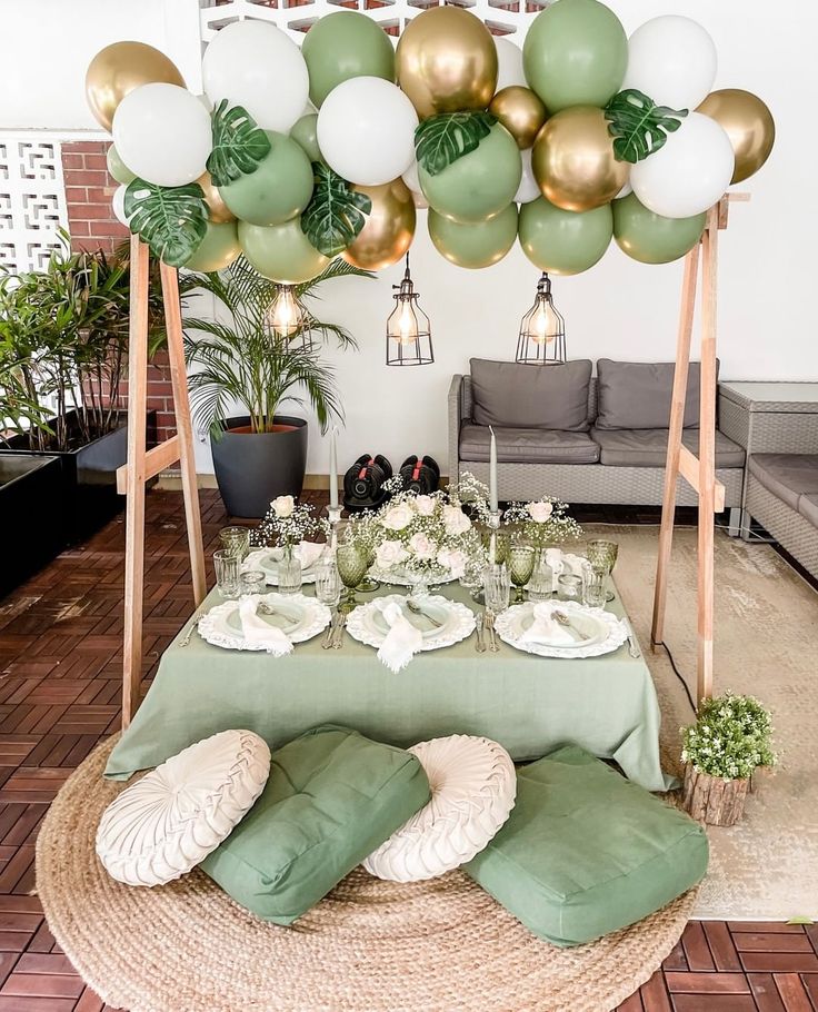 the table is set up with green and white balloons, plates and silverware on it