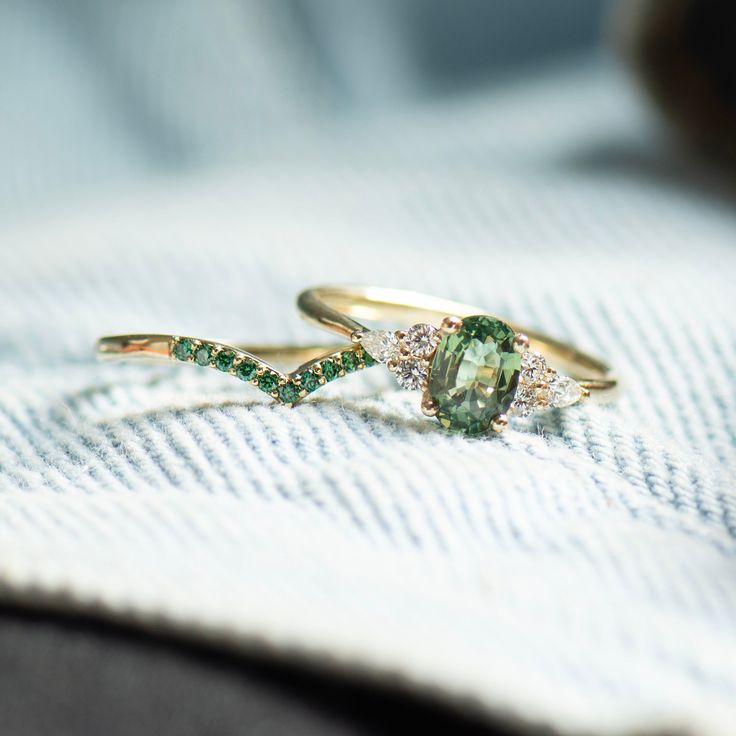 two gold rings with green and white stones on them sitting on top of a towel