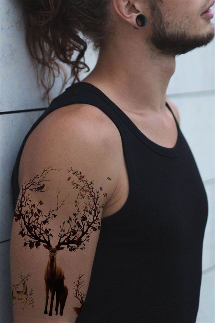 a man with a deer tattoo on his arm next to a white wall and tree