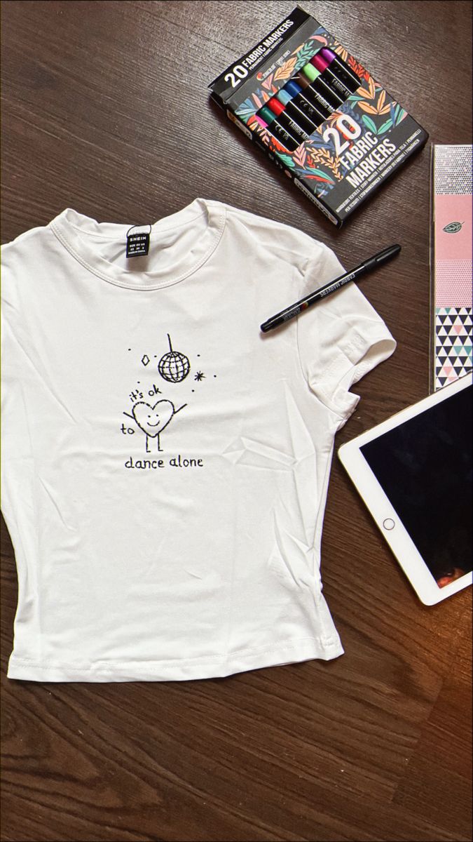 a white t - shirt that says to dance alone next to a tablet and pen