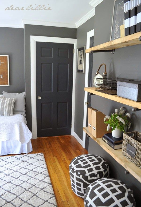 a bedroom with gray walls and white bedding, black door and shelves on the wall