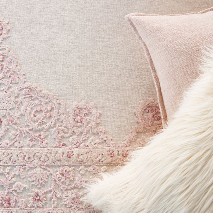 a pink and white pillow sitting on top of a bed next to a fur covered pillow