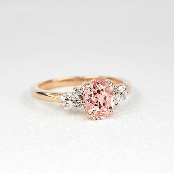 a pink diamond ring with three diamonds on the band and an oval shaped center stone