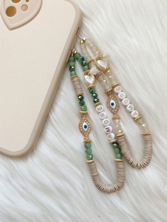 three beaded bracelets are next to a cell phone on a white furnish