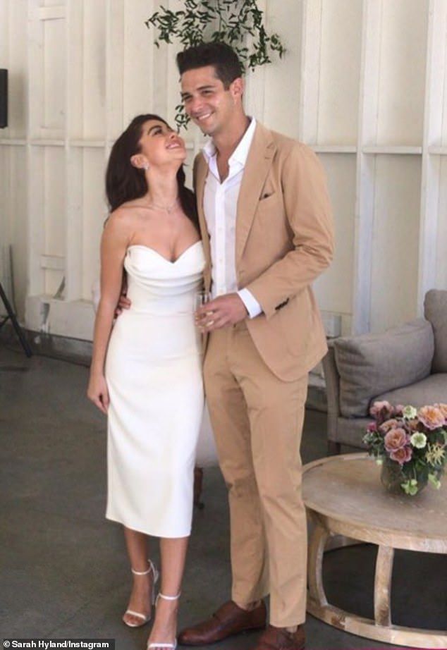 a man and woman standing next to each other in front of a white wall with flowers