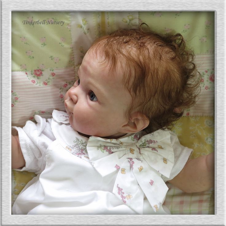 a baby laying on top of a bed wearing a white dress with flowers and bows