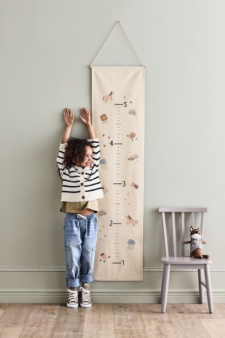 a little boy standing in front of a growth chart with his hands on the wall