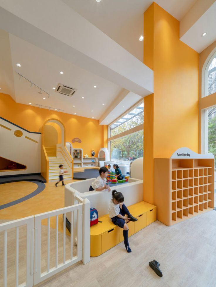 two children playing in a play room with yellow walls and white stairs, while another child plays on the floor