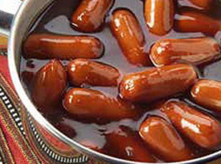 several hot dogs are in a tin with sauce on it and one is being cooked