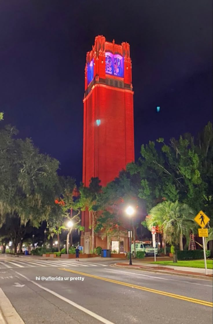 a red clock tower lit up in the night sky with trees and street lights around it