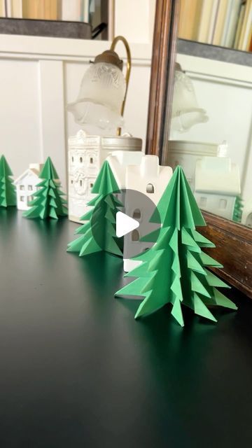 some paper trees sitting on top of a table next to a mirror and a lamp