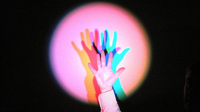 a person holding up a multicolored hand in front of a bright light ball