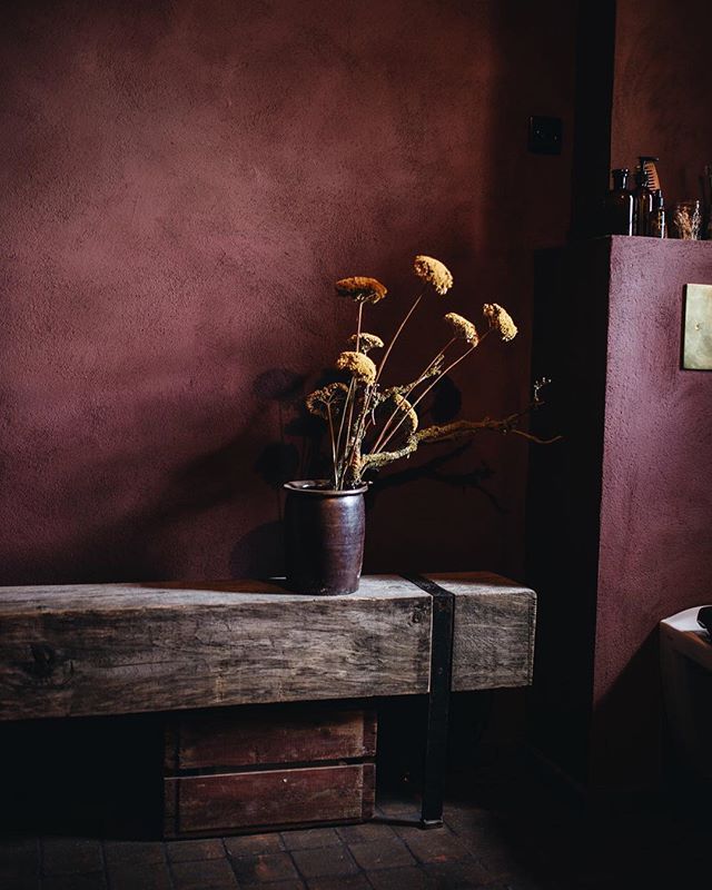 a wooden bench sitting in front of a purple wall with dried flowers on top of it