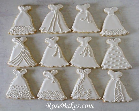 twelve decorated cookies in the shape of wedding gowns and tiaras on a table