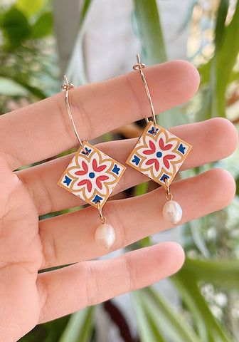 a hand holding a pair of earrings with flowers and pearls on the end of it