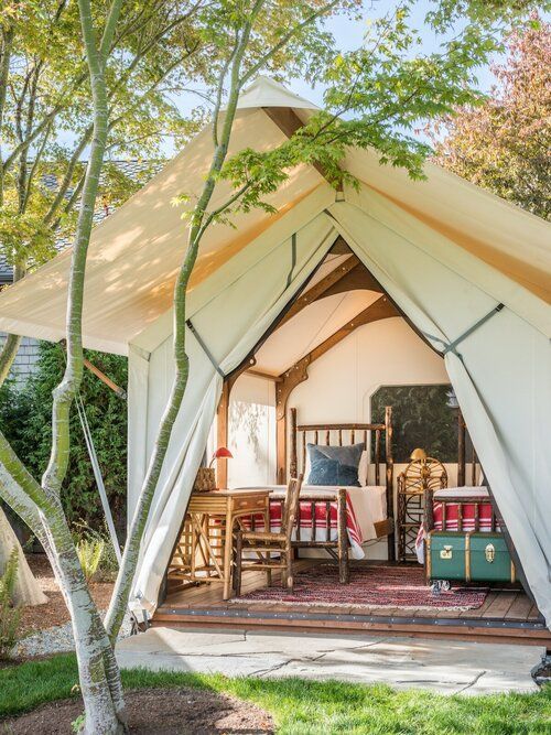 a white tent with two beds in it and some trees outside the tent is surrounded by grass