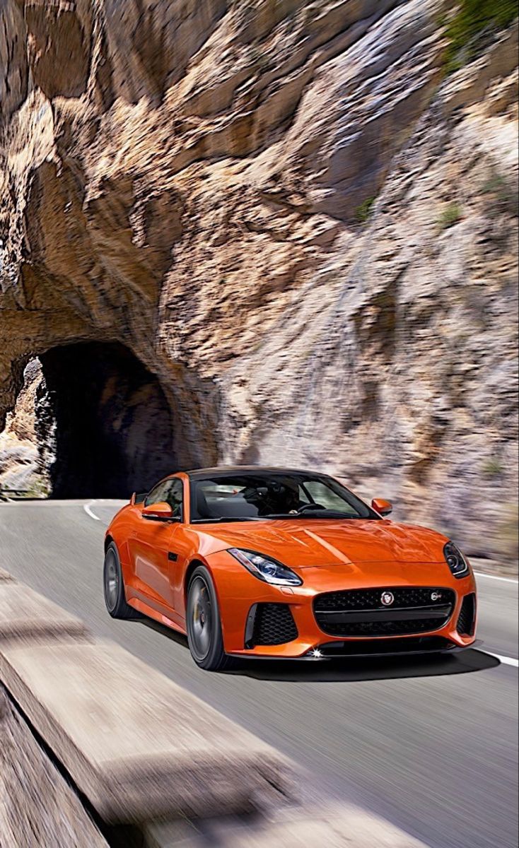 an orange sports car driving through a tunnel on the road in front of a mountain