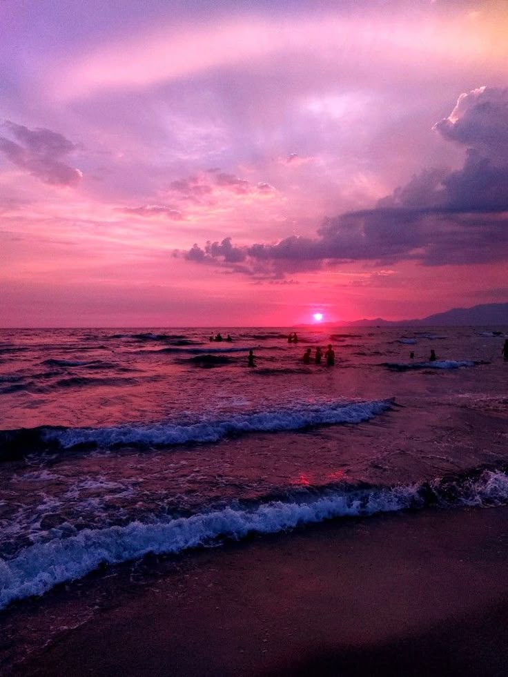 the sun is setting over the ocean and people are in the water