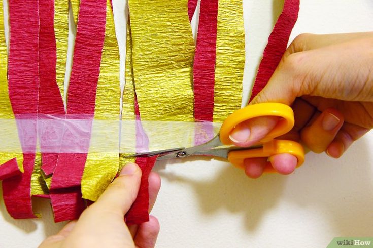 someone cutting paper with scissors on top of a piece of material that is red and yellow