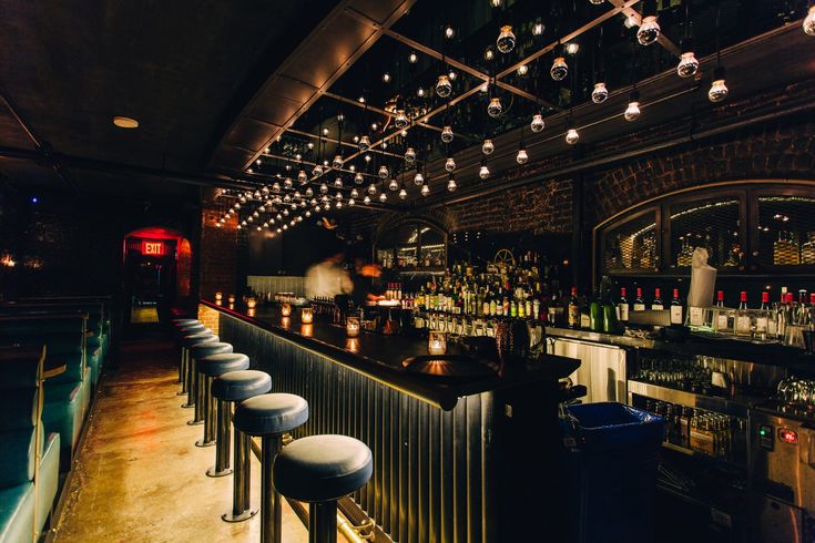 a dimly lit bar with several stools and lights hanging from the ceiling above it