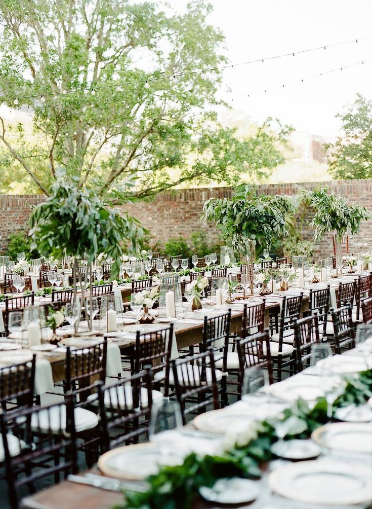 tables set up for an outdoor wedding with greenery and white linens on them