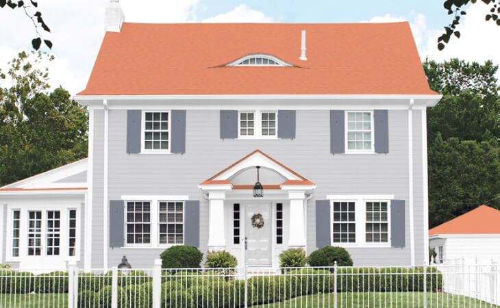 a large gray house with red roof and white fence