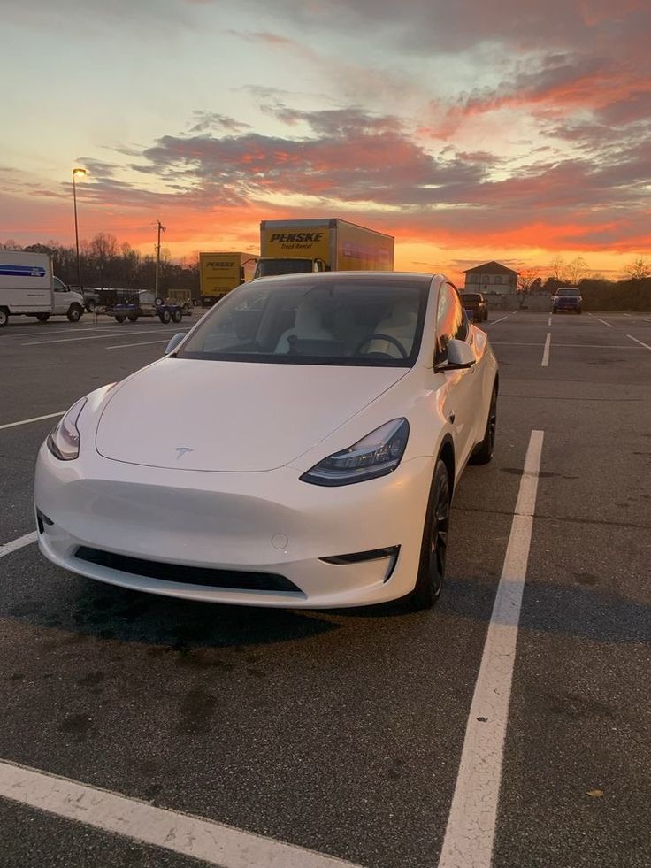 a white electric car parked in a parking lot at sunset with the sun setting behind it