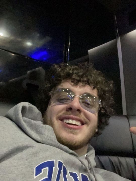 a man with curly hair and glasses is smiling at the camera while sitting in a car