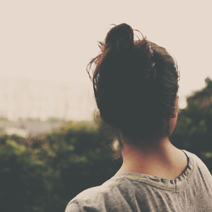 the back of a woman's head with her hair in a bun, looking out over trees