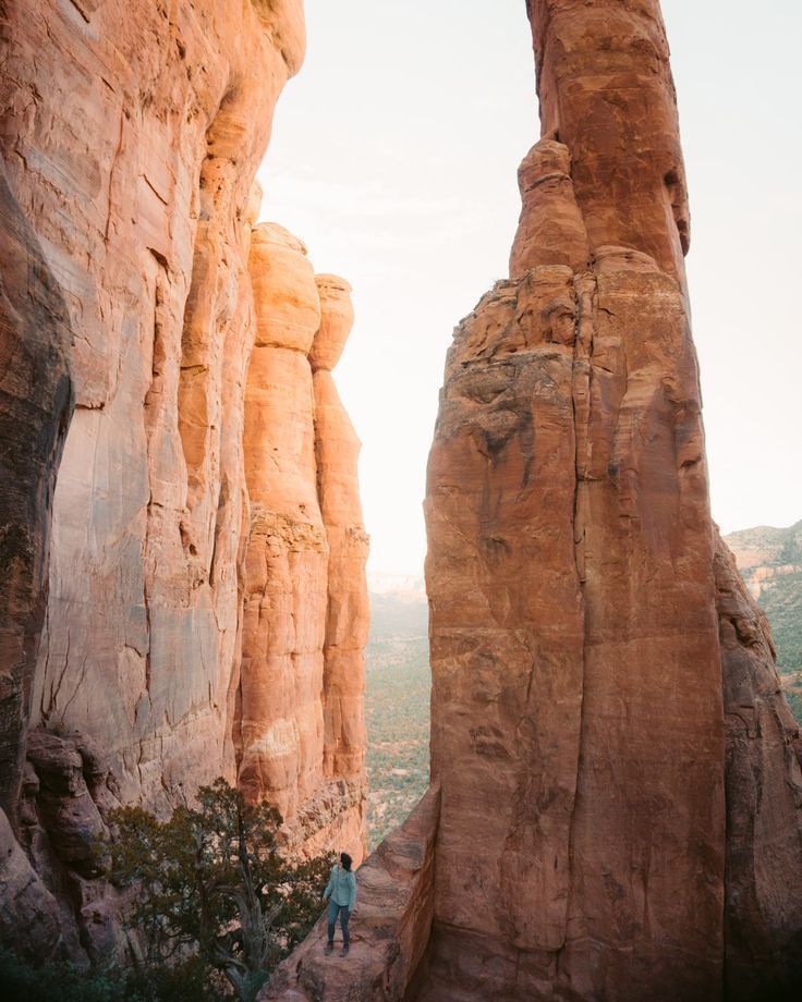 a person standing in between two large rocks on the side of a mountain with an arch