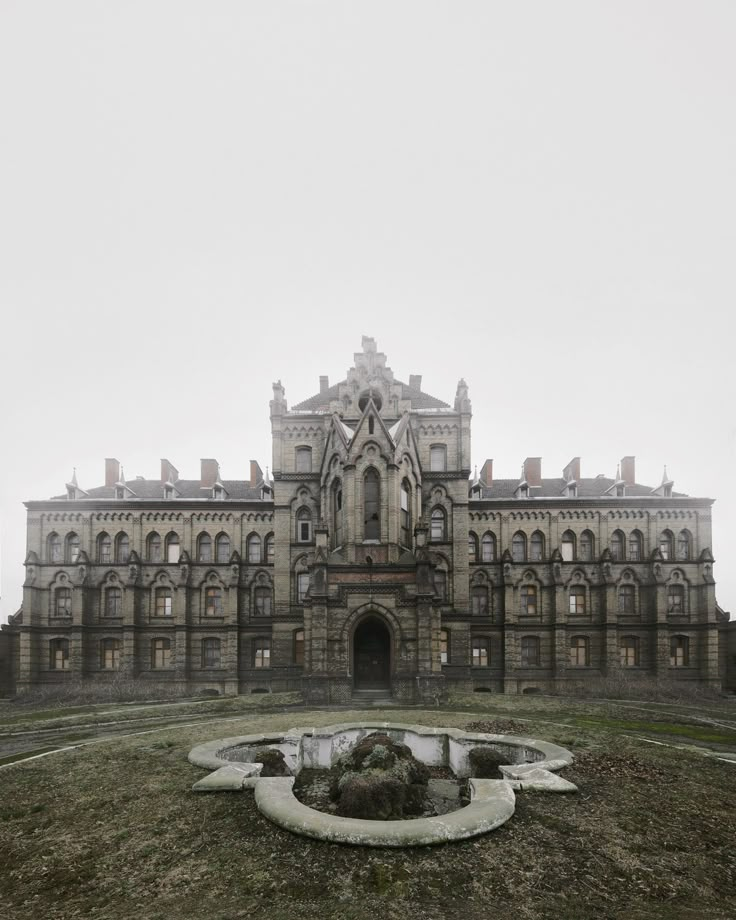 an old building with a fountain in front of it on a foggy, overcast day