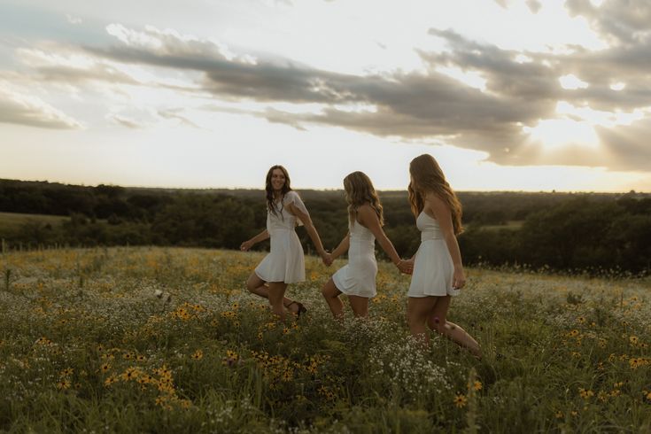 three girls in white dresses walking through a field