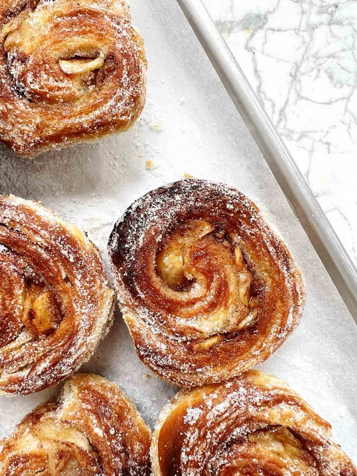 several cinnamon rolls on a baking sheet covered in powdered sugar