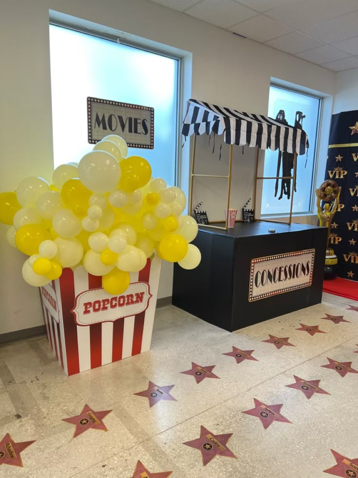 a popcorn box filled with yellow balloons sitting on top of a tiled floor next to stars