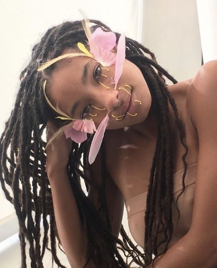 a woman with dreadlocks and pink flowers on her head posing for the camera