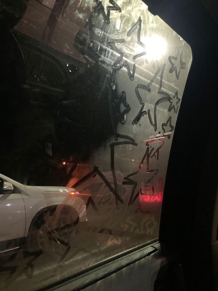 graffiti on the side of a car window in front of a white vehicle with its door open