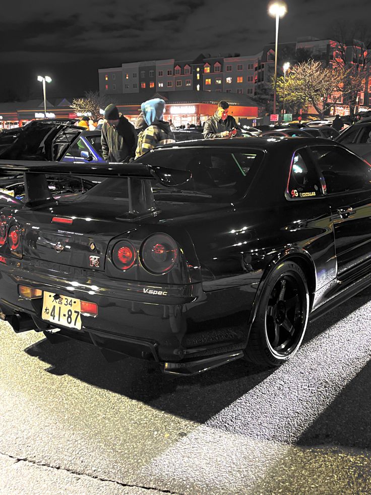 several cars parked in a parking lot with people standing around them at the back end