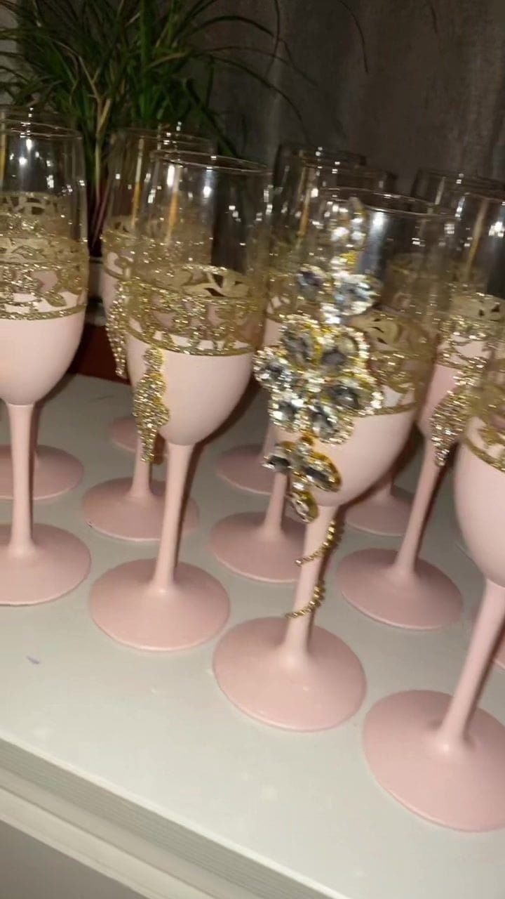 pink and gold wine glasses lined up on top of each other in front of a potted plant