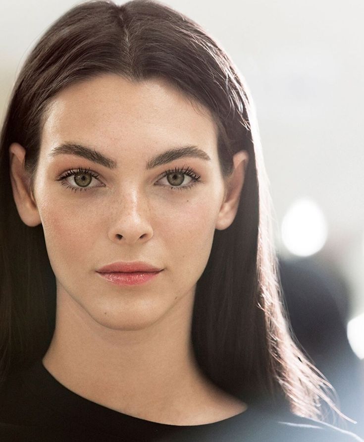 a woman with long black hair and green eyes looks at the camera while wearing a black top