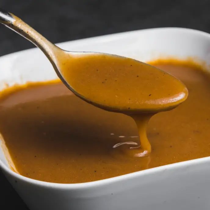 a spoon full of caramel sauce in a white bowl with a black tablecloth