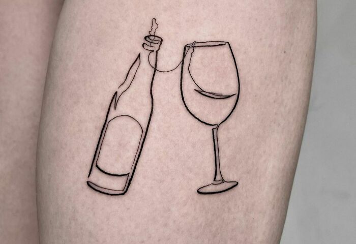 a wine glass and bottle tattoo on the side of a woman's thigh,